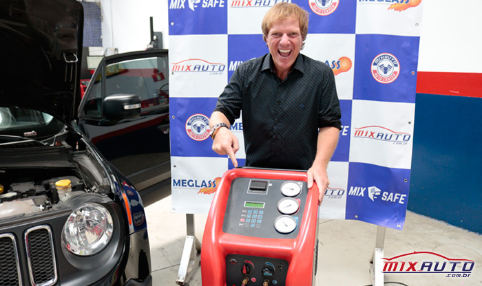Apresentador Ciro Bottini apontando para o aparelho que realiza a carga de gás do ar condicionado automotivo